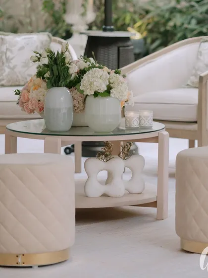 A chic and modern lounge setting with quilted pastel ottomans and elegant white sofas. The floral arrangements are kept simple and clean, complementing the contemporary furniture.