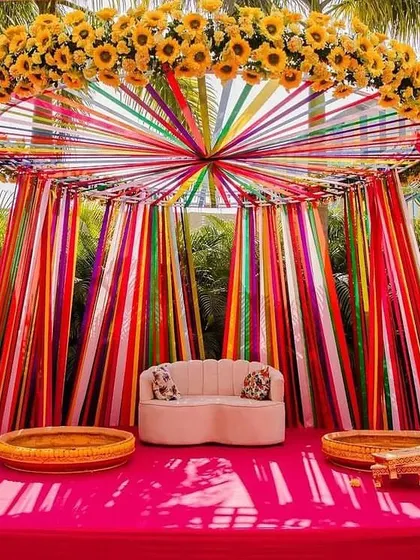 A fun and colorful Haldi stage with a canopy of rainbow ribbons. The design is playful and modern, perfect for a high-energy celebration.