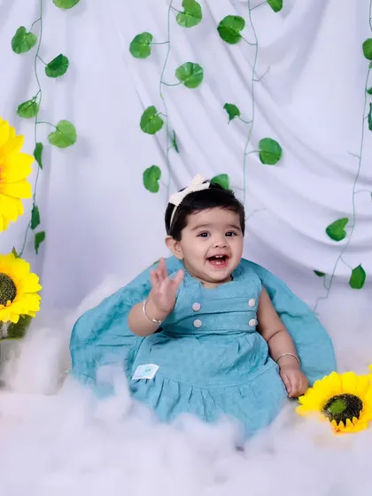 A joyful baby girl waving at the camera during her sunflower-themed sitter session.