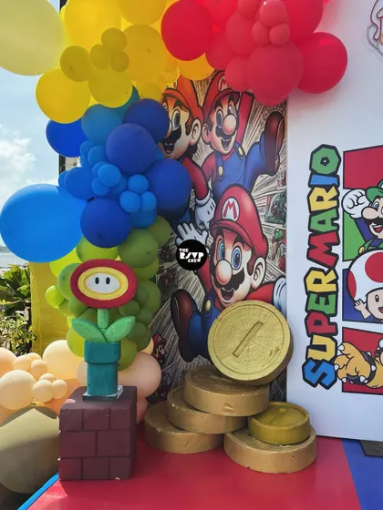 A close-up of the Super Mario decor, showing a fire flower prop, a stack of gold coins, and a vibrant balloon garland.