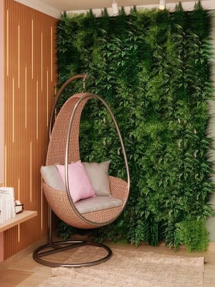 A comfortable swing chair is perfectly complemented by a dense artificial fern wall behind it. This setup creates a peaceful and stylish indoor retreat, perfect for relaxing with a book.
