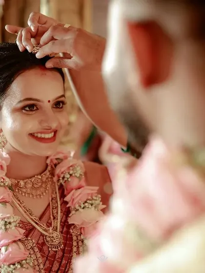 The groom applies sindoor to the bride's hair parting, a significant and beautiful ritual in a Hindu wedding, captured in an intimate over-the-shoulder shot.
