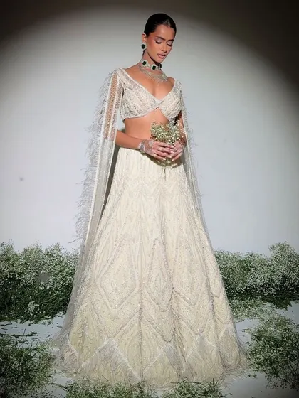 An ivory lehenga embellished with delicate pearls and intricate craftsmanship, paired with a blouse featuring dramatic feathered sleeves.