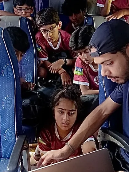 A coach uses a laptop on the team bus for video analysis with the players. Learning happens everywhere, not just on the pitch.