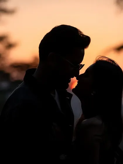 A close-up silhouette of a near-kiss, capturing the anticipation and intimacy of the moment against the soft colors of the sunset.