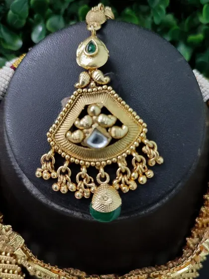 A close-up of a maang tikka with an antique gold finish, part of a temple jewellery set.