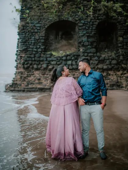 A candid moment of a couple sharing a look by the ruins on a beach.