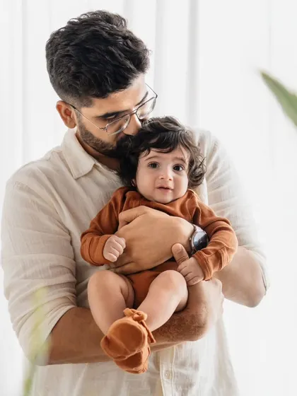 A father holds his baby boy close. The soft, natural light from the window creates a serene and loving mood for this portrait.