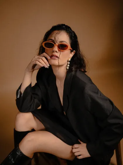 A close-up from the 'FLOR' series, adding a pop of color with orange sunglasses. This shows how a single accessory can change the mood of a monochromatic outfit.