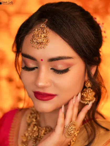 A close-up beauty shot of a model, her eyes closed to showcase the flawless makeup. The traditional gold jewelry and her serene expression create a look of pure elegance.