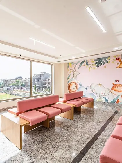 This pediatric waiting area at Sarvesh Health City features a large window for natural light and a charming wall mural. The comfortable, low-to-the-ground seating is scaled for children and their families.