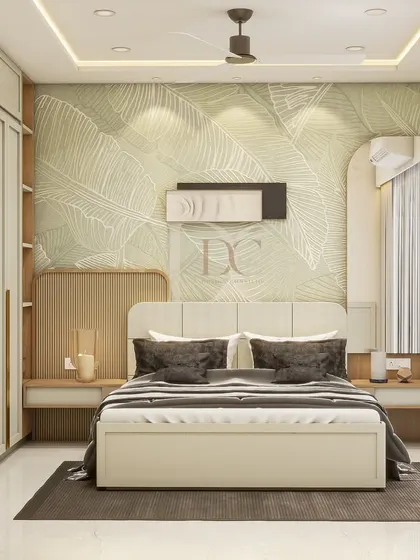 Luxury is a feeling, and it starts in the bedroom. This design for a villa in Mira Road features a soft green botanical wallpaper, a comfortable upholstered bed, and a sleek wardrobe with integrated open shelves.