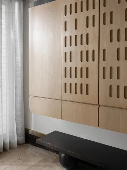 A custom floating shoe cabinet with a unique perforated pattern on the doors, paired with a minimalist black bench. This piece combines modern design with practical storage.