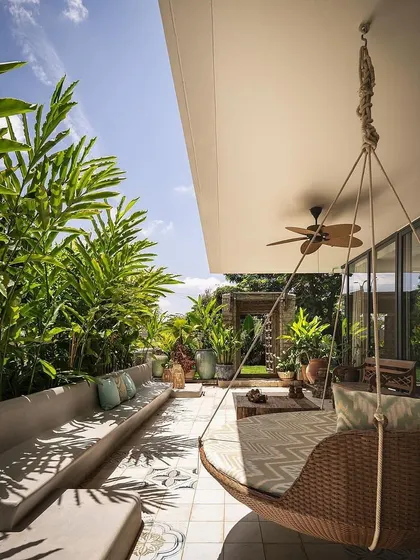 This covered patio at Embassy Boulevard features built-in concrete seating and a hanging swing chair, surrounded by dense greenery to create a comfortable and private outdoor living room.