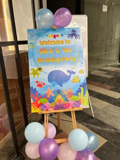 A welcoming entrance for a first birthday party. This 'Under the Sea' themed welcome sign on an easel, adorned with balloons, sets the perfect tone for guests.