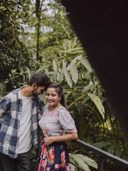 A candid and romantic shot of a couple from their pre-wedding shoot, framed by lush green leaves.