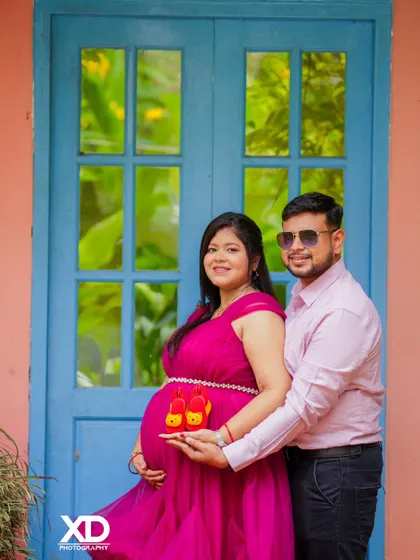A sweet close-up of a couple holding baby shoes, with a colorful blue door in the background.