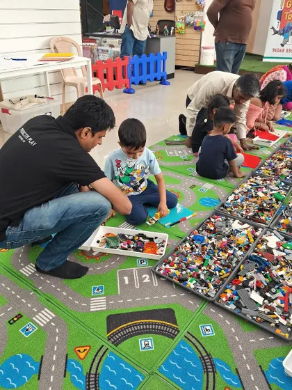 A father helps his son with a LEGO creation on a playmat designed like city roads. This setup encourages imaginative play and storytelling alongside the building activity.