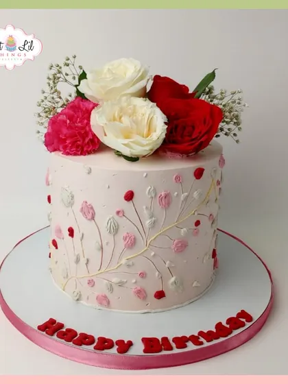 An elegant birthday cake with delicate, hand-piped floral branches and topped with fresh red and white roses.