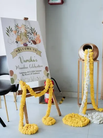 This traditional welcome setup for a Mundan celebration combines a personalized welcome board with a decorative pot overflowing with marigold flowers, creating a warm and auspicious vibe.