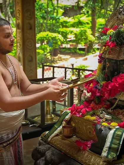 A priest performs aarti to the Ganesha idol, which is surrounded by lush greenery. The natural setting of our temple adds to the serene and spiritual ambiance.