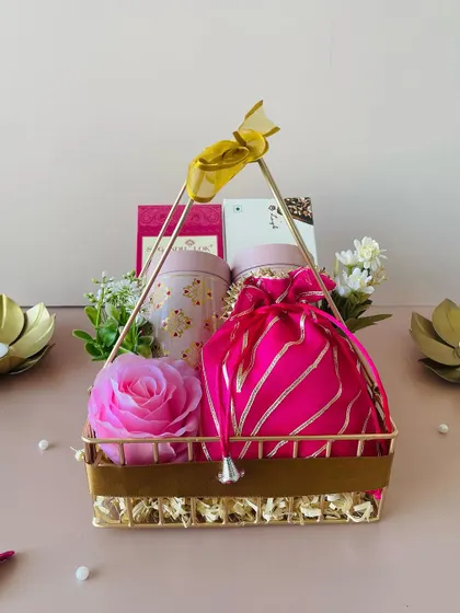This elegant gold metal basket is curated with pink-themed items, including a decorative rose and a silk potli, creating a luxurious and feminine gift.