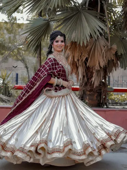A joyful shot of a bride twirling in a beautiful off-white lehenga with a contrasting maroon dupatta. The movement creates a dynamic and celebratory feel.