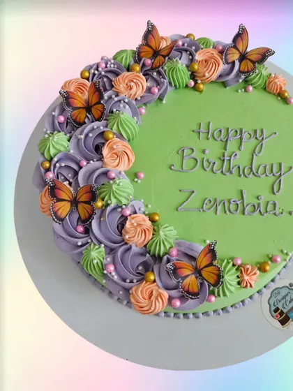 A green birthday cake with a crescent of orange, purple, and green flowers, accented with monarch butterflies. The color combination is unique and beautiful.