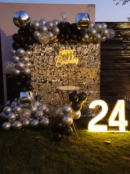 A chic outdoor setup for a 24th birthday, using a silver sequin wall, black and silver balloons, and light-up numbers.