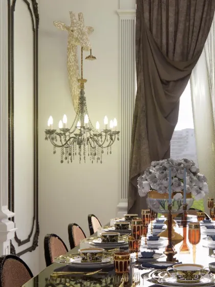 A dining experience defined by classical grandeur. This space features a quirky giraffe-head wall sconce holding a crystal chandelier, ornate wall mouldings, and a beautifully set table, creating a whimsical yet elegant ambiance.