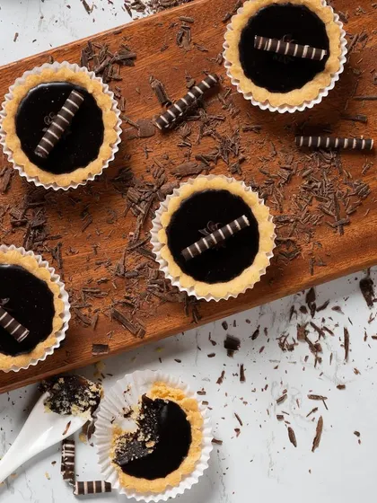 An overhead shot of our mini chocolate tarts, decorated with chocolate curls and shavings. This showcases the clean, elegant presentation of our patisserie selection.