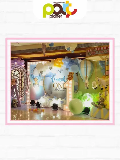 A full view of a whimsical first birthday stage, featuring hot air balloons, a large light-up number one, and adorable teddy bear details.