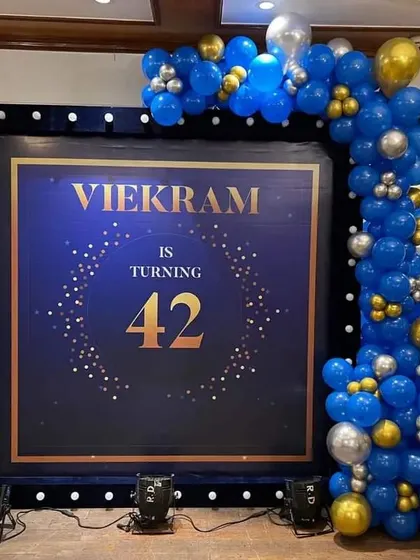 An elegant and modern setup for a 42nd birthday party. The deep blue and gold theme, complete with a custom digital backdrop and a stylish balloon arch, is perfect for a sophisticated celebration.