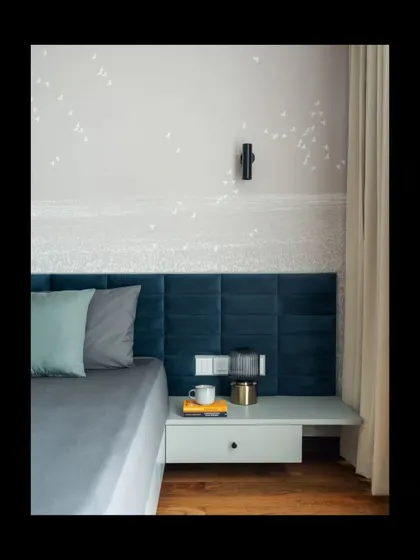 In this bedroom, a custom deep blue velvet headboard provides a touch of color and texture against a serene, hand-painted wallpaper depicting a distant shoreline. The floating nightstand and minimalist wall sconce maintain the room's clean lines, crafting a space that feels both elegant and deeply restful.