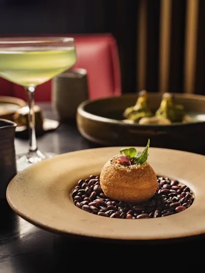 An elegantly plated appetizer in a fine-dining setting. The moody lighting and shallow depth of field draw attention to the dish's unique presentation on a bed of beans.