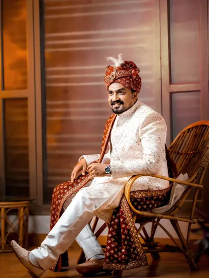 A classic groom portrait, seated and looking relaxed in his traditional sherwani and turban.