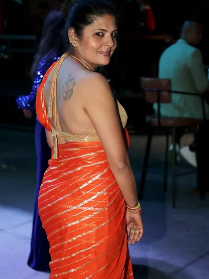 A backless halter-neck blouse in gold shimmer fabric, designed to be the highlight of this orange striped saree look.