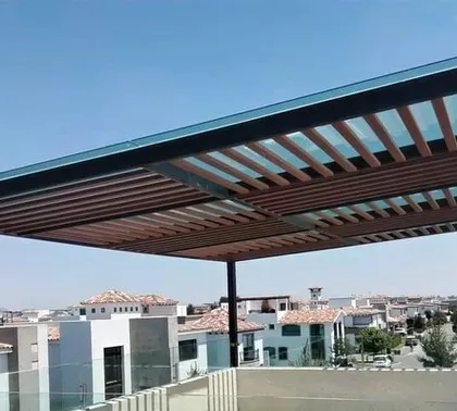 A sleek, modern pergola design featuring a metal frame and a glass roof with wooden-finish slats. This design offers a contemporary look while providing partial shade, ideal for sunny Bangalore afternoons.