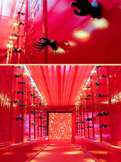 A bold and enchanting entrance for a 'Red Room' themed Sangeet. The corridor is bathed in red light, with unique hand sculptures lining the walls, creating a dramatic and immersive experience from the very first step.