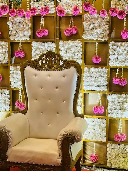 A close-up of a pink and white themed backdrop for a baby shower. The checkerboard design is made with panels of white flowers, with hanging pink floral tassels adding a delicate touch.