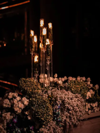 A detail of a floral and candle arrangement against a dark background. The contrast highlights the delicate structure of the flowers and the warm, flickering light, showcasing our focus on creating a moody and atmospheric event.