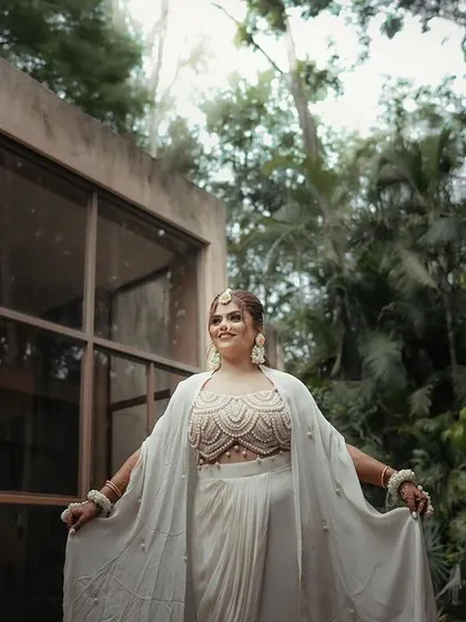 A bride in a modern white outfit, her arms outstretched in a moment of freedom and joy. The lush green background adds to the fresh, happy feeling of the shot.