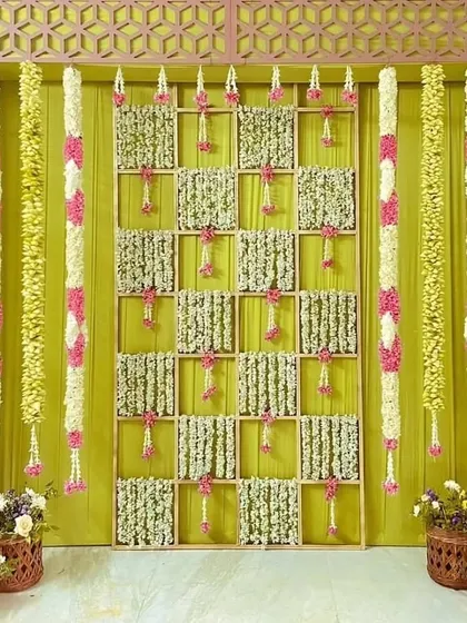 A unique baby shower backdrop featuring a lattice frame with panels of jasmine flowers. The hanging floral strings and side garlands add color and texture to the design.