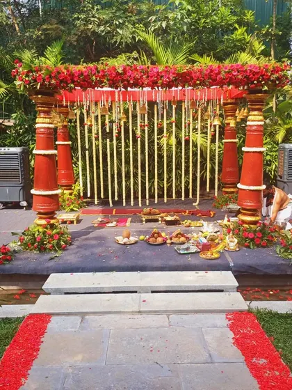 A beautiful stone path lined with red petals leading to a traditional red-pillared mandap.