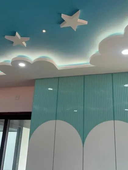 A whimsical kids' room featuring a cloud-and-star themed false ceiling and a two-tone wardrobe. The design is both playful and practical, with plenty of storage and space to play.