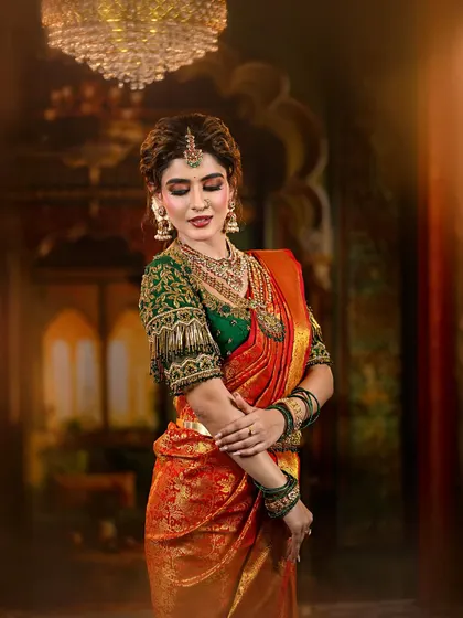 A regal and traditional bridal look featuring a rich red and green Kanjivaram saree. The makeup is defined by warm, shimmery eyes and a deep red lip, perfectly accessorized with temple jewelry.