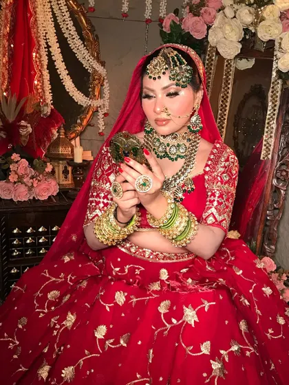 The bride's final check in the mirror. This look highlights the rich red and gold embroidery of the lehenga with makeup that is equally detailed and luxurious.