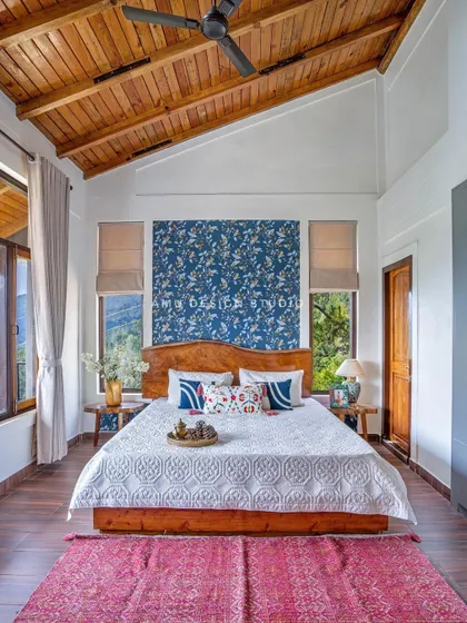 The master bedroom in 'The Mountain Home,' featuring a high, wood-paneled ceiling, a custom solid wood bed, and a bold blue floral wallpaper accent that brings the beauty of nature indoors.