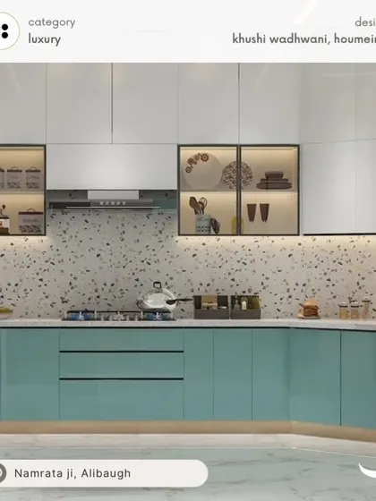 This kitchen design showcases a beautiful blend of modern and classic elements. The teal blue lower cabinets provide a pop of color, while the white upper cabinets keep the space feeling bright and airy. The terrazzo backsplash and glass-fronted crockery units with internal lighting add a touch of luxury and sophistication.