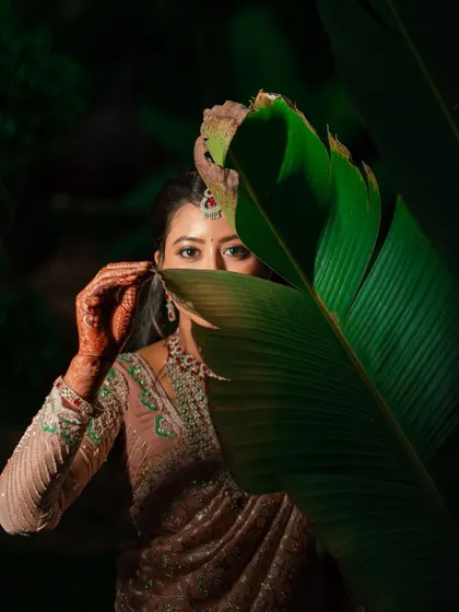 An artistic portrait of the bride peeking from behind a large green leaf, a creative and playful shot.